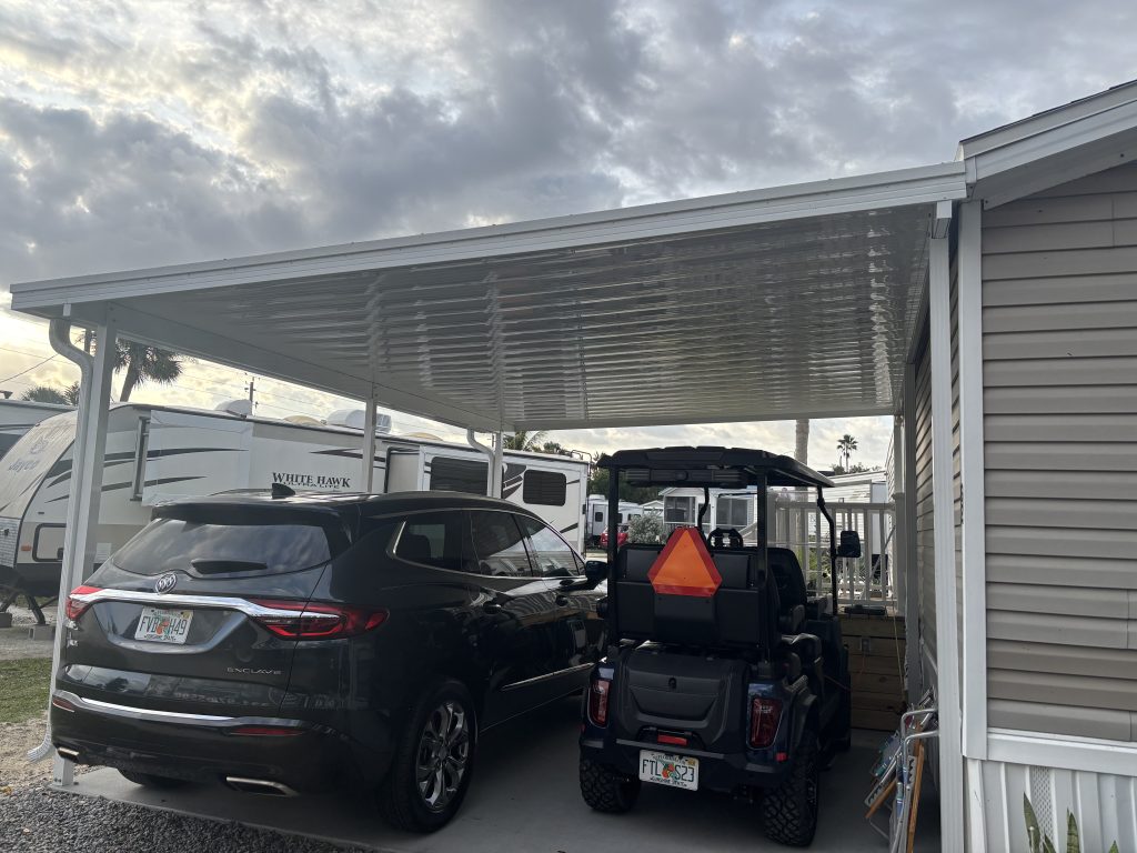 White aluminum carport with vehicles parked underneath showing corrugated roof panels