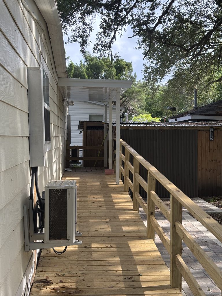White aluminum 18-foot by 16-foot carport with ground-set posts beside an existing screen room at a Merritt Island, Florida mobile home park, sized for two compact vehicles
