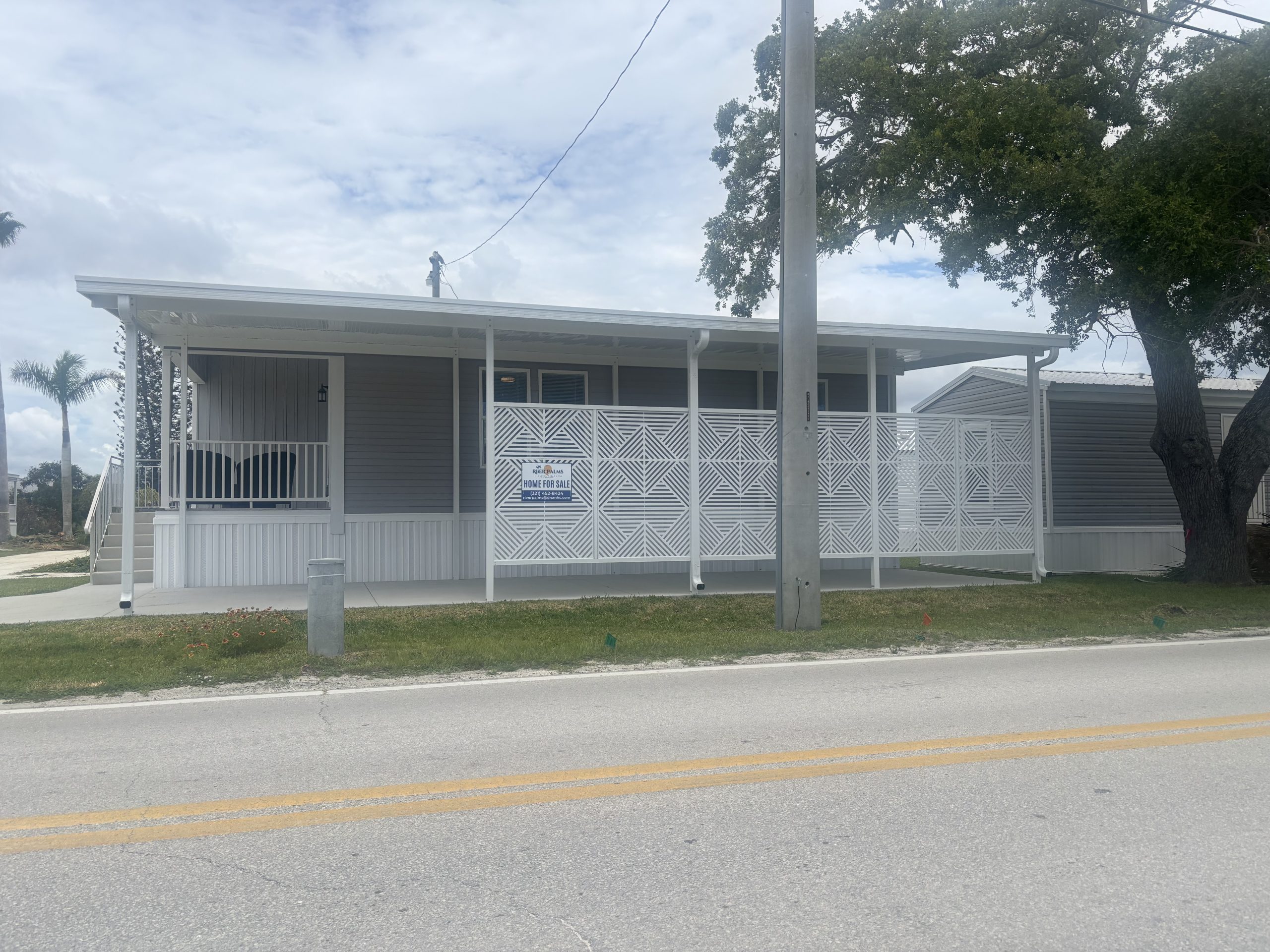 White aluminum pan roof carport with 4th wall construction built beside a new mobile home in Merritt Island, Florida, with a privacy fence installed along one side